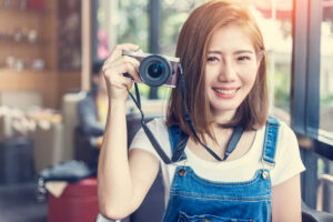 右手でカメラを持って微笑む茶髪のアジア人女性