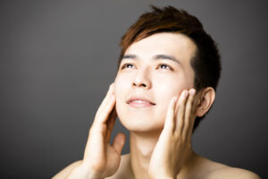 天を仰いで化粧水を塗り込むアジア人男性