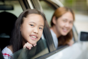 後部座席から外に顔を出す女の子と運転席のお母さん
