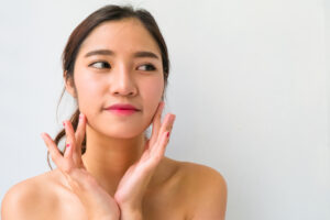 両手の人差し指ででスキンケア用品を頬に塗るひっつめ髪のアジア人女性